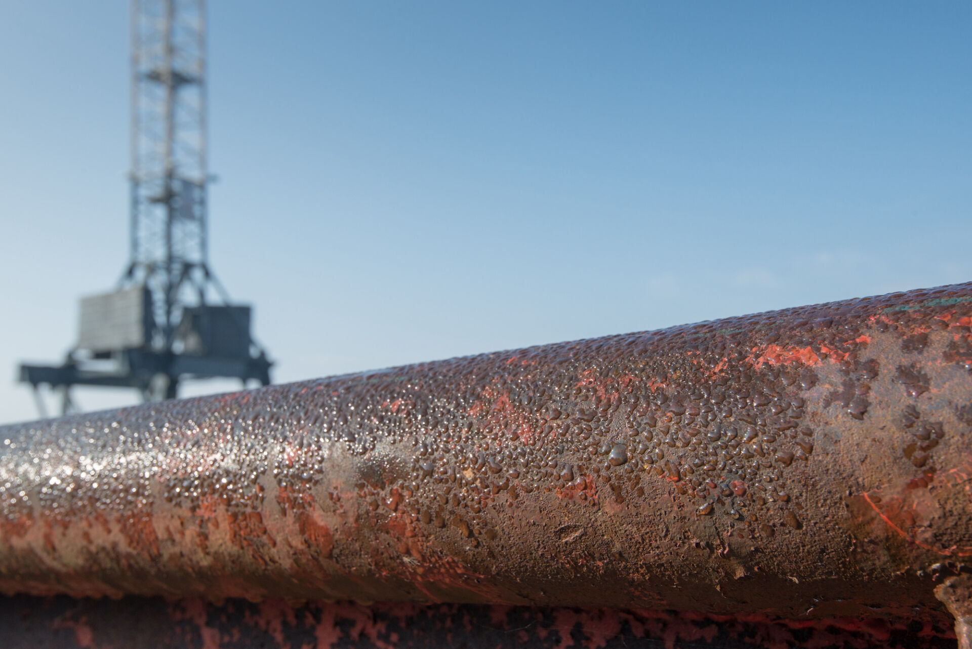 Close-up of a corroded marine pipeline with an offshore rig in the background, highlighting biofilm-induced corrosion challenges in the energy sector
